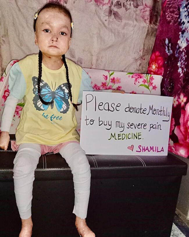 Shamila holding a sign asking for monthly donations for pain medicine